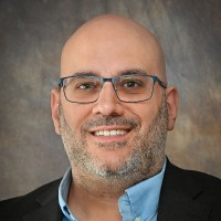 smiling bald man wearing a suit coat and button-up shirt with black-rimmed glasses and a salt and pepper beard and mustache