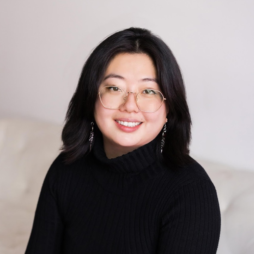 smiling women with black hair and clear-rim glasses, wearing a black shirt and dangling earrings