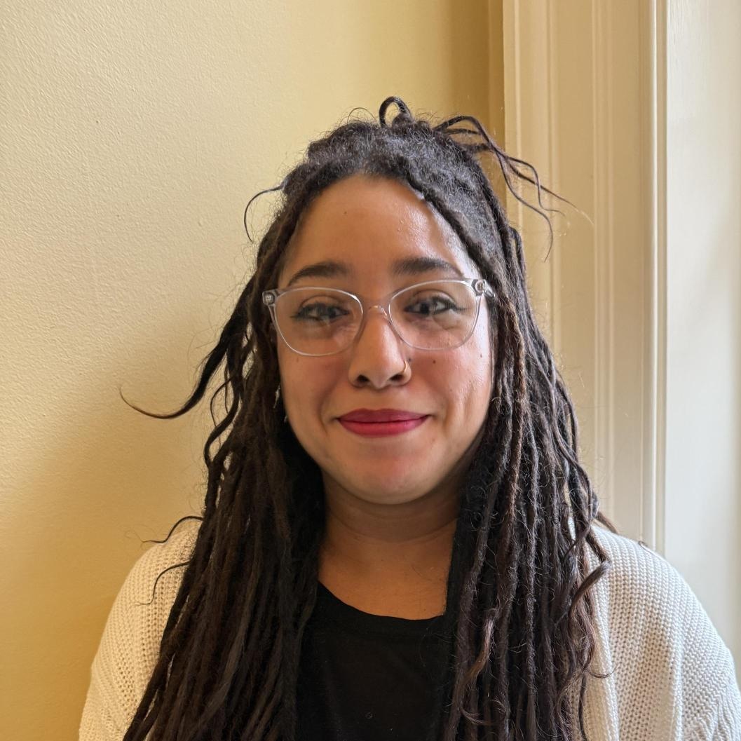 smiling women with black braided hair and clear-rim glasses, wearing a black shirt and off-white cardigan